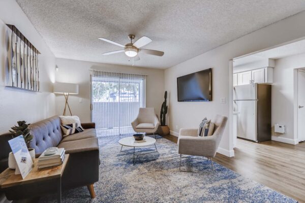 Latitude apartment living room with plush seating, pattern rug, ceiling fan, and balcony door.