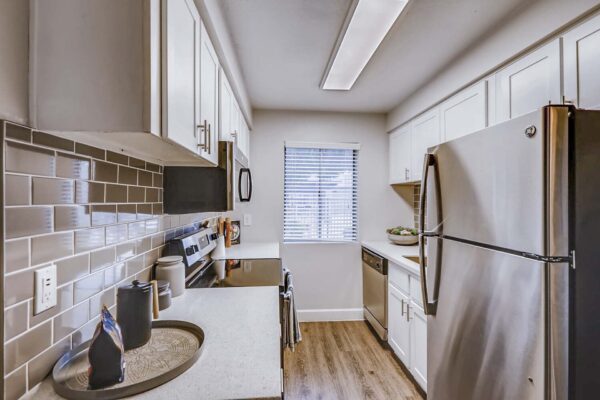 Latitude apartment kitchen with wood style floor, white cabinets and counters, tiled backsplash, and stainless steel appliances.