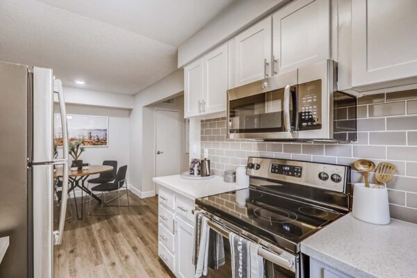 Latitude apartment kitchen with wood style floor, white cabinets and counters, tiled backsplash, and stainless steel appliances.