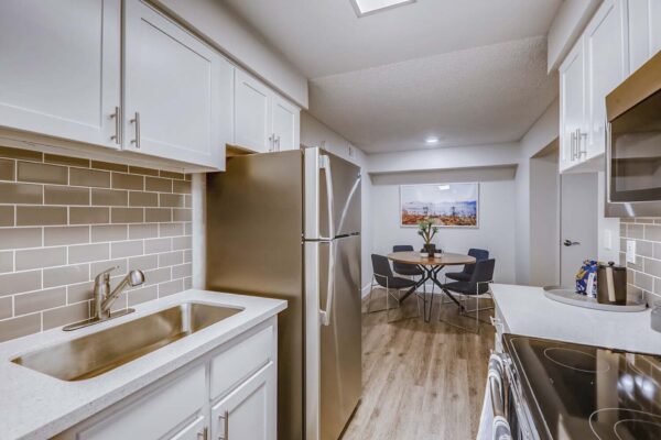 Latitude apartment kitchen with wood style floor, white cabinets and counters, tiled backsplash, and stainless steel appliances.