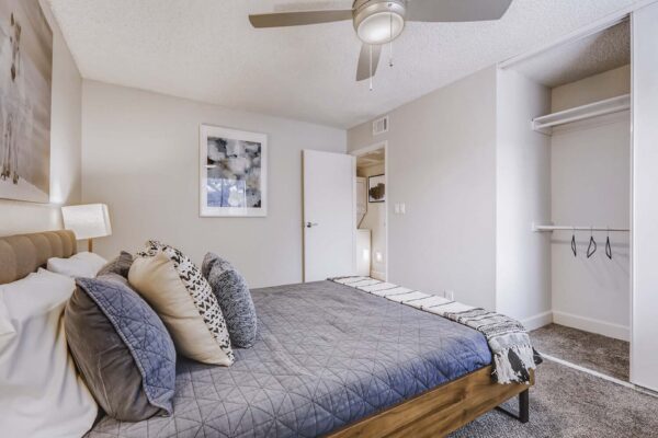 Latitude apartment bedroom with plush carpet, bed with headboard, ceiling fan, and closet.