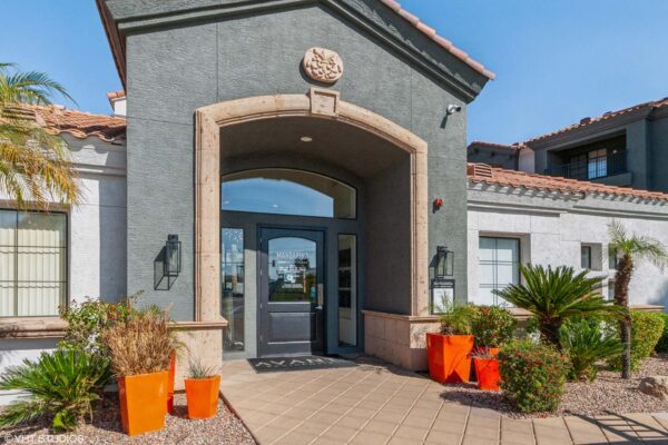 Mandarina apartments clubhouse entrance with lush landscaping and large archway.