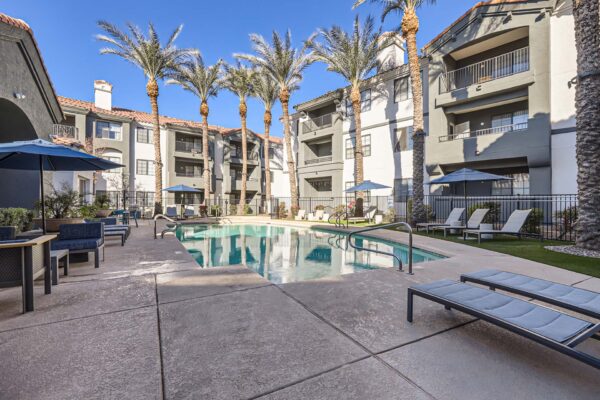 Mandarina apartments pool area with lounge chairs, dining tables, and tall palm trees.