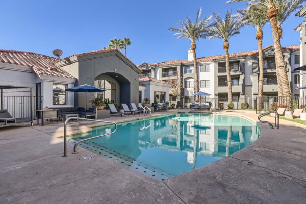 Mandarina apartments pool area with lounge chairs, umbrellas, and tall palm trees.