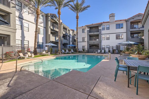 Mandarina apartments pool area with dining table, lounge chairs, and tall palm trees.