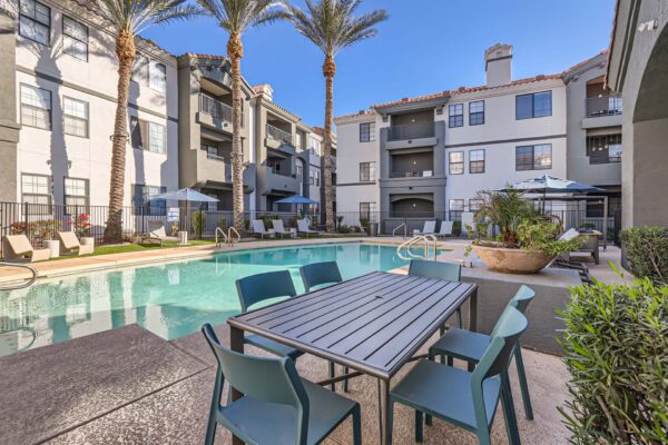 Mandarina apartments pool area with dining table, lounge chairs, and tall palms.