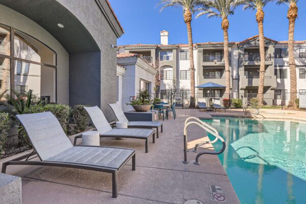 Mandarina apartments pool area with lounge chairs and tall palm trees.