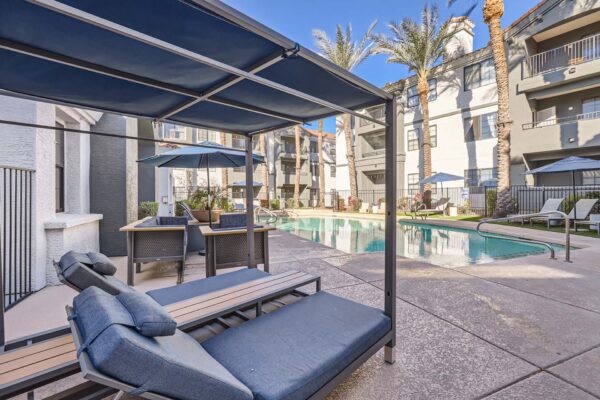 Mandarina apartments pool area with covered lounge chairs and tall palm trees.