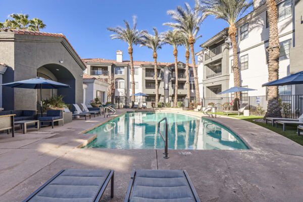 Mandarina apartments pool area with lounge chairs, umbrellas, and tall palm trees.