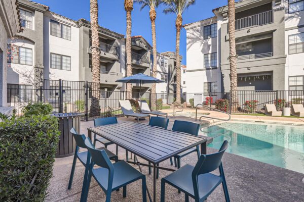 Mandarina apartments pool area with dining table, lounge chairs, and tall palms.