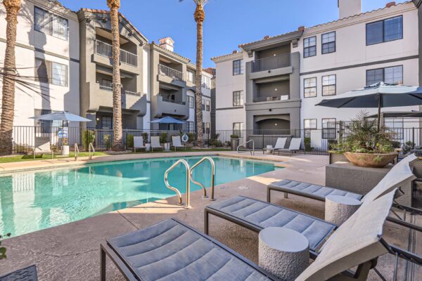 Mandarina apartments pool area with lounge chairs, planters with flowers, and tall palm trees.
