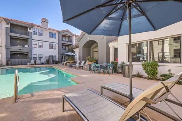 Mandarina apartments pool area with lounge chairs, umbrellas, and dining table.