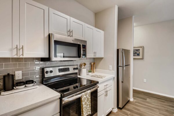 Mandarina apartment kitchen with wood style floor, white cabinets and counters, and stainless steel appliances.