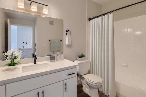 Mandarina apartment bathroom with white cabinets and counters, large mirror, and tiled shower tub.