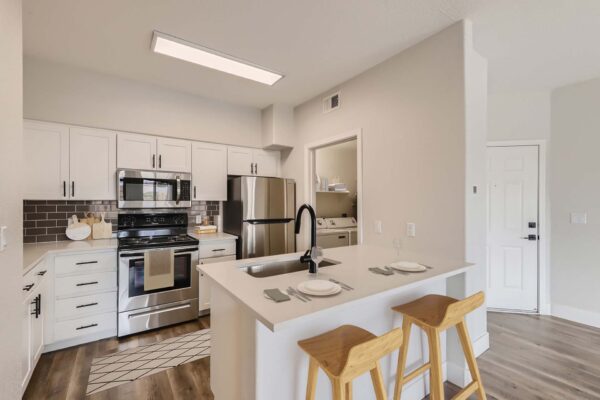 Mandarina apartment kitchen with wood style floor, white cabinets and counters, and stainless steel appliances.