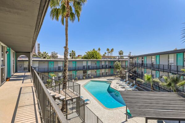 Omnia on Thomas apartments pool area with lounge chairs, pergola, and tall palm trees.