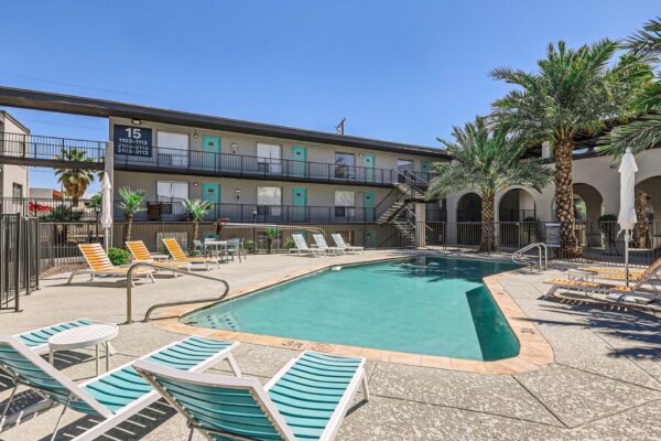 Omnia on Thomas apartments pool area with lounge chairs and tall palm trees.