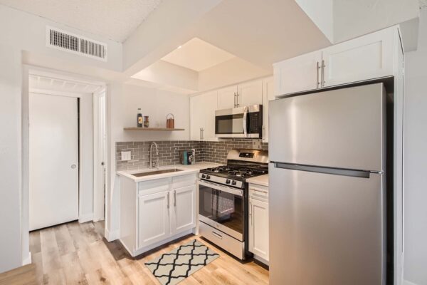 Omnia on Thomas apartment kitchen with wood style floor, white cabinets and counters, and stainless steel appliances.