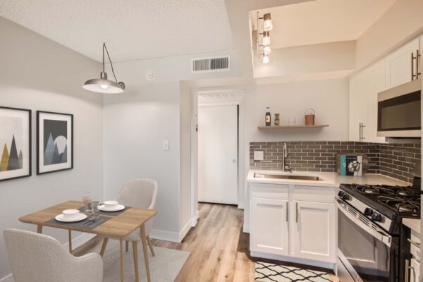 Omnia on Thomas apartment kitchen with wood style floor, white cabinets and counters, stainless steel appliances, and dining table.