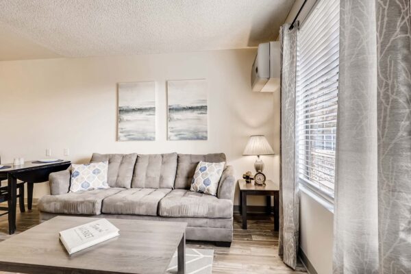 Overlook at Sunset Point apartment living room with plush couch, dining table, artwork, and large window.