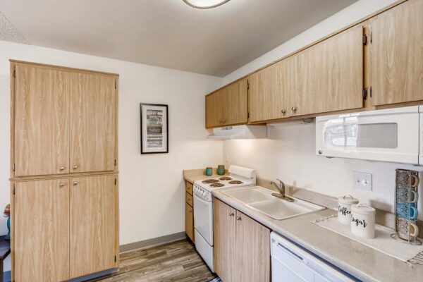 Overlook at Sunset Point apartment kitchen with wood style floor and cabinets, light counters, and white appliances.