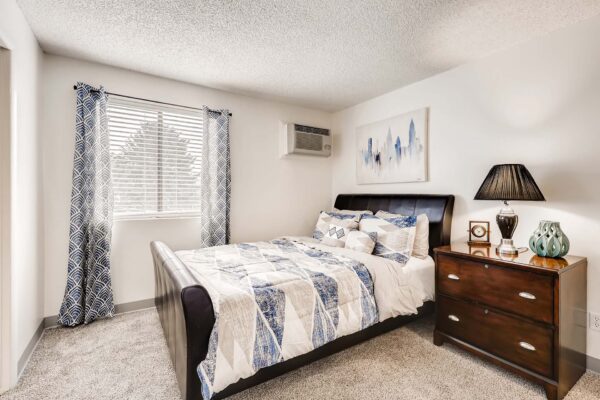 Overlook at Sunset Point apartment bedroom with carpet, plush bed with headboard, bedside drawers with lamp, and large window.