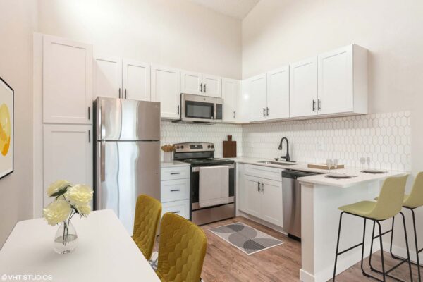 Overlook at Sunset Point apartment kitchen with wood style floor, white cabinets and counters, stainless steel appliances, and dining table.