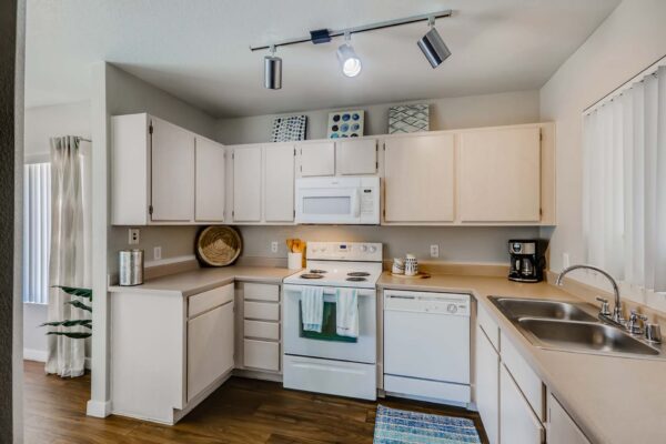 Pavilions at Arrowhead apartment kitchen with wood style floor, light cabinets and counters, and white appliances.