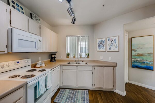 Pavilions at Arrowhead apartment kitchen with wood style floor, light cabinets and counters, and white appliances.