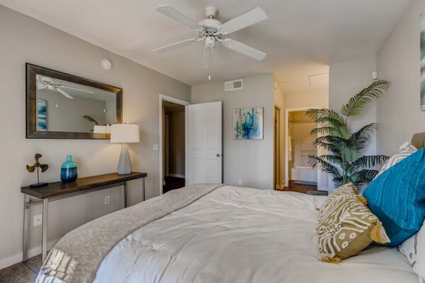 Pavilions at Arrowhead apartment bedroom with plush bed, large framed mirror, and ceiling fan.