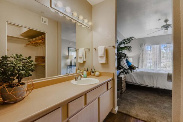 Pavilions at Arrowhead apartment bathroom with wood style floor, tan cabinets and counters, and large mirror.