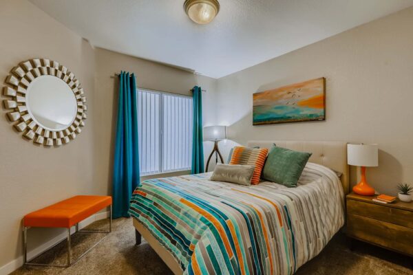 Pavilions at Arrowhead apartment bedroom with carpet, plush bed with headboard, and large window.