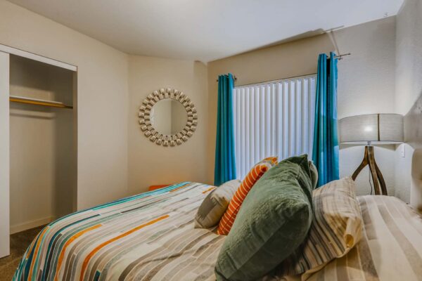 Pavilions at Arrowhead apartment bedroom with plush bed, large lamp, round mirror, and closet.