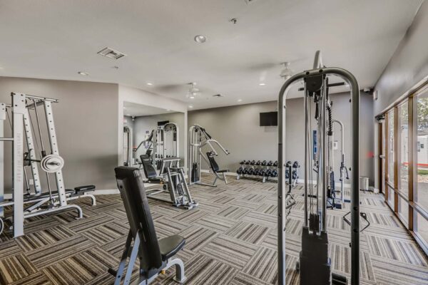 Pavilions at Arrowhead apartments fitness center with weight equipment and large windows.