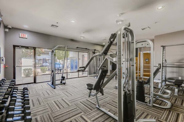 Pavilions at Arrowhead apartments fitness center with weight machines and large windows.