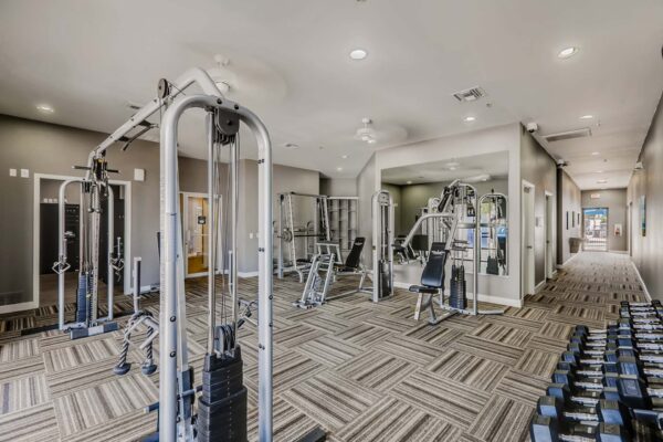 Pavilions at Arrowhead apartment fitness center with weight machines and large mirror.