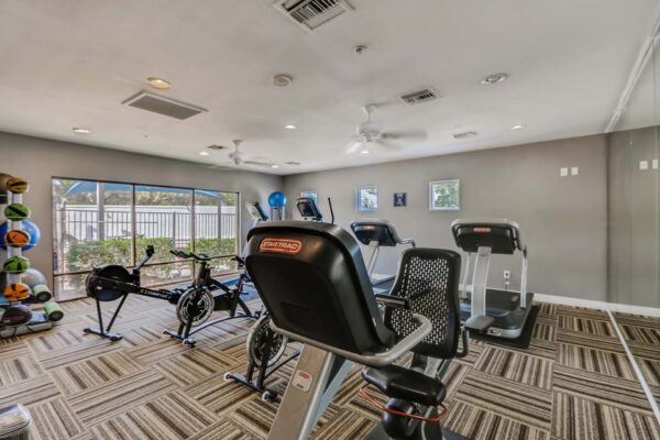 Pavilions at Arrowhead apartments fitness center with cardio machines and large windows.