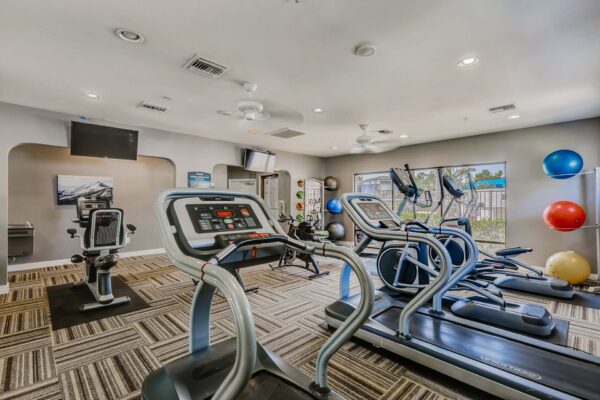 Pavilions at Arrowhead apartments fitness center with cardio machines and TVs.