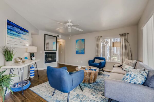 Pavilions at Arrowhead apartment living room with colorful rug, plush seating, fireplace, and large windows.