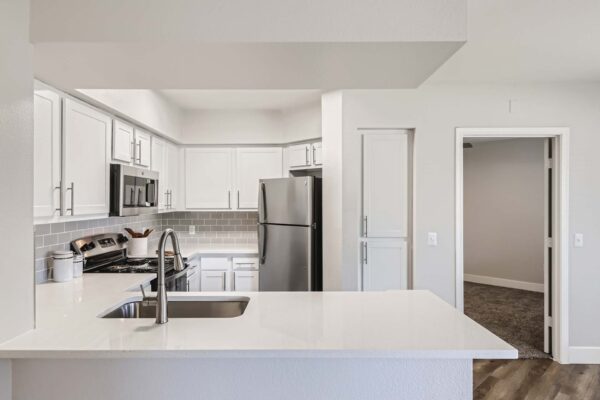 Pavilions at Arrowhead apartment kitchen with wood style floor, white cabinets and counters, and stainless steel appliances.