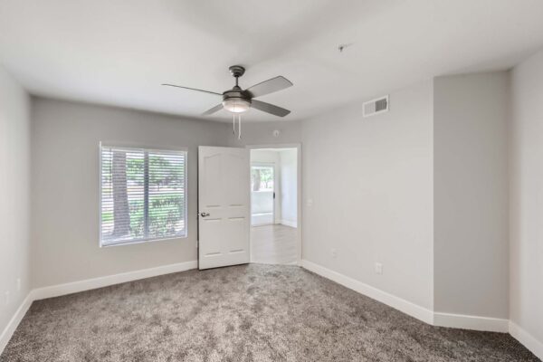 Pavilions at Arrowhead apartment bedroom with plush carpet, ceiling fan, and large window.