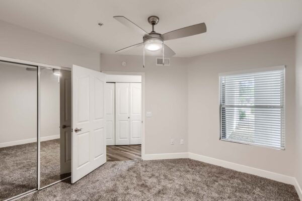 Pavilions at Arrowhead apartment bedroom with plush carpet, ceiling fan, and closet.