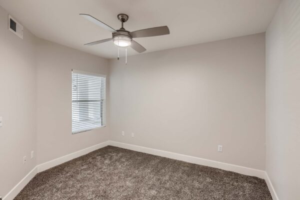 Pavilions at Arrowhead apartment bedroom with plush carpet, ceiling fan, and large window.