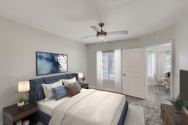 Pavilions at Arrowhead apartment bedroom with carpet, plush bed with headboard, ceiling fan, and large windows.