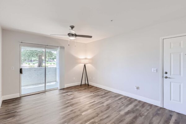 Pavilions at Arrowhead apartment living room with wood style floor, ceiling fan, lamp, and balcony door.
