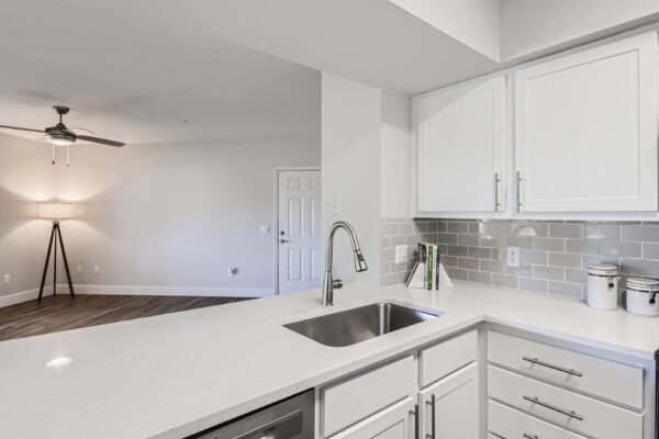 Pavilions at Arrowhead apartment kitchen with white cabinets and counters, tiled backsplash, and stainless steel sink.