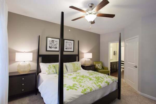 Prairie View at Village West apartment bedroom with four post bed, bedside drawers with lamps, and ceiling fan.