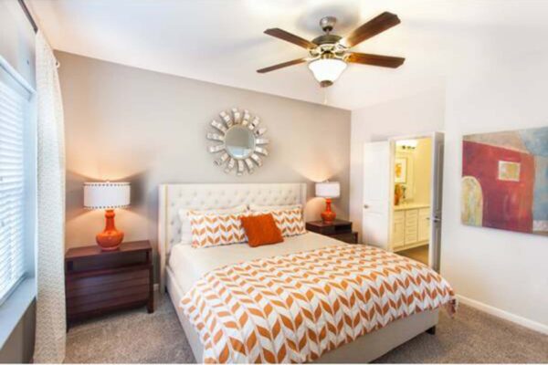 Prairie View at Village West apartment bedroom with plush carpet, bed with headboard, and bedside drawers with lamps.
