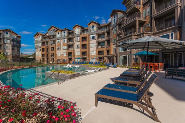 Prairie View at Village West apartments pool area with lounge chairs, umbrellas, and lush flowers.