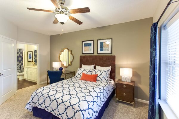Prairie View at Village West apartment bedroom with plush carpet, large bed with headboard, and bedside tables with lamps.